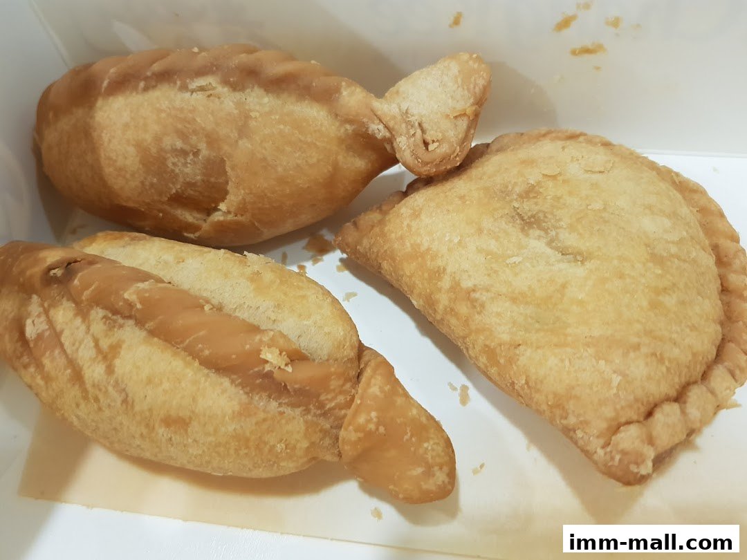 Three golden-brown pastries, two sausage rolls and one curry puff, in a white box.