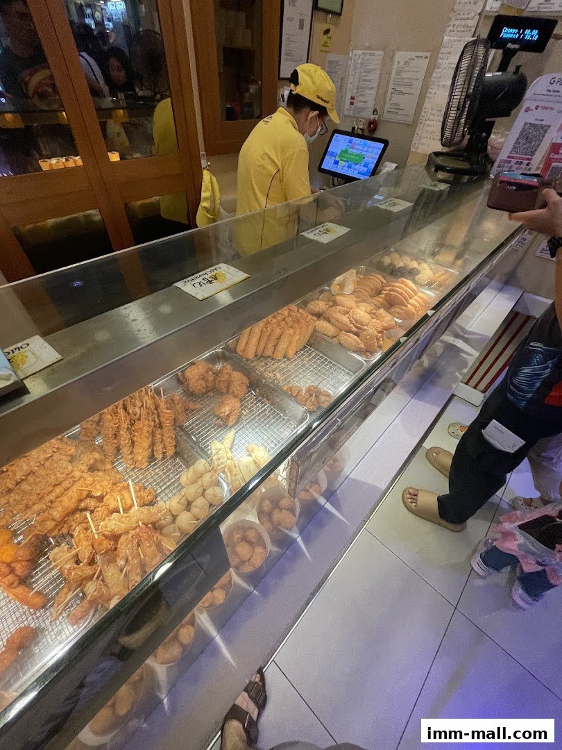 A display case filled with various fried snacks at Old Chang Kee, with a staff member behind the counter.