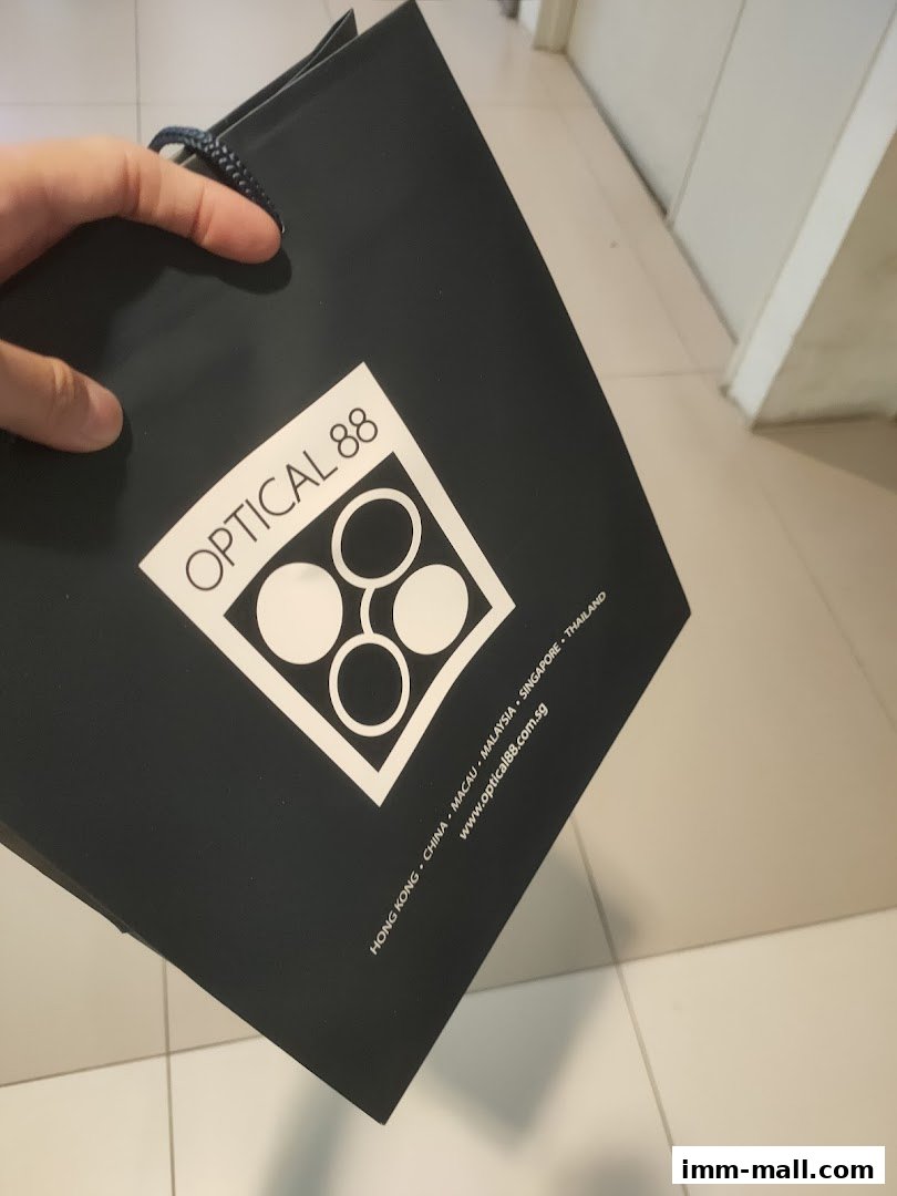 A hand holds a black shopping bag with the Optical 88 logo and website.