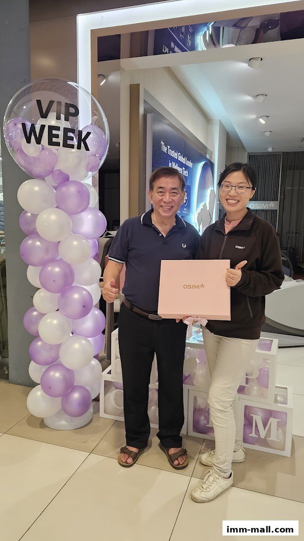 Two people smiling and holding an OSIM gift box in front of balloons and store displays.
