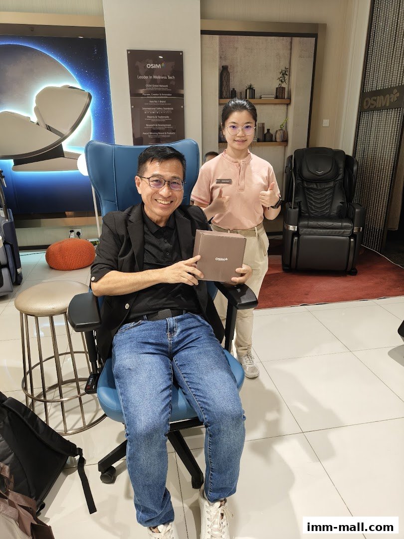 A man sits in a massage chair while a woman stands beside him, both smiling.