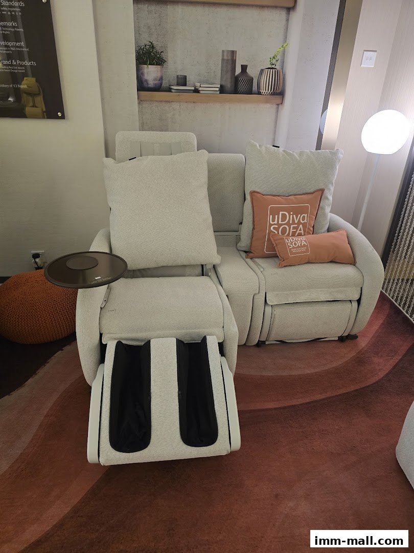 A modern massage chair with footrest and decorative pillows is displayed in a well-lit retail space.
