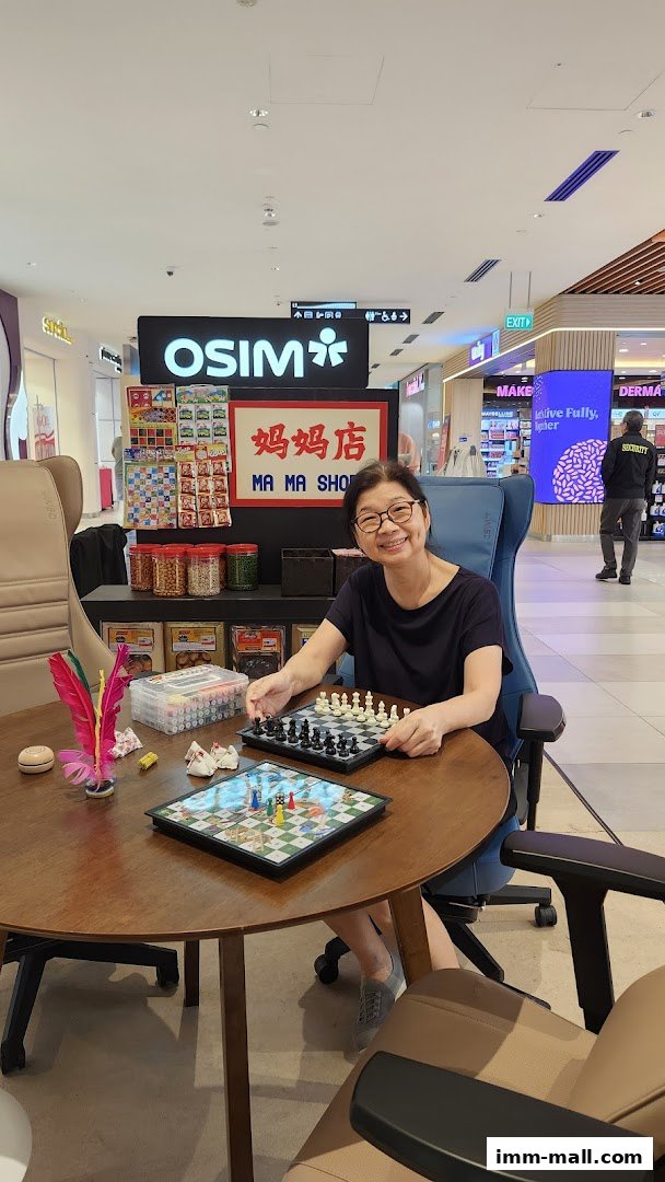 A woman plays chess at a table in front of an OSIM store with various products displayed.