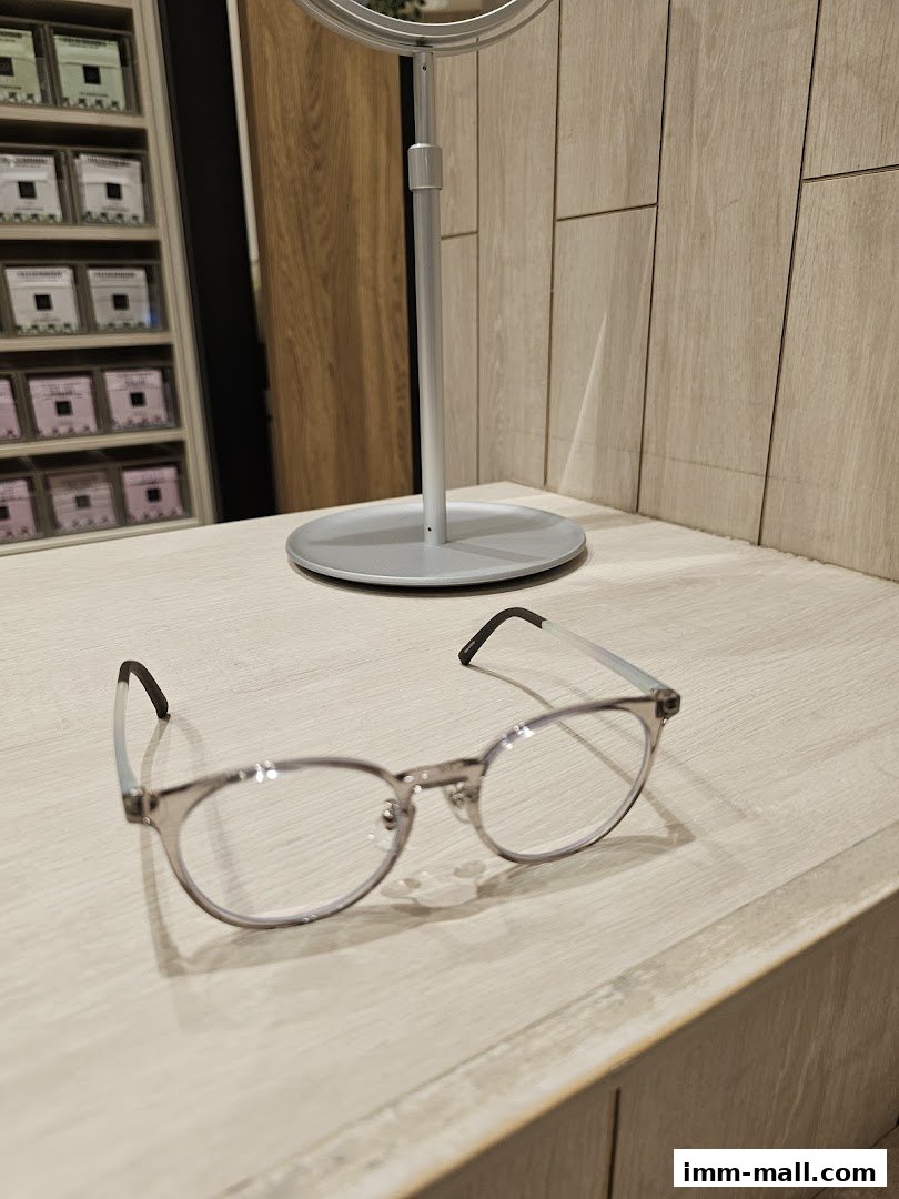 A pair of stylish eyeglasses rests on a wooden surface in front of a mirror.