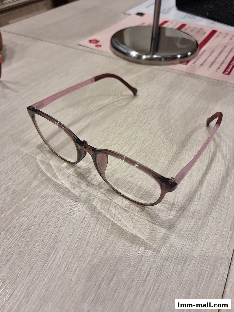 A pair of stylish eyeglasses with pink temples rests on a light wooden surface.