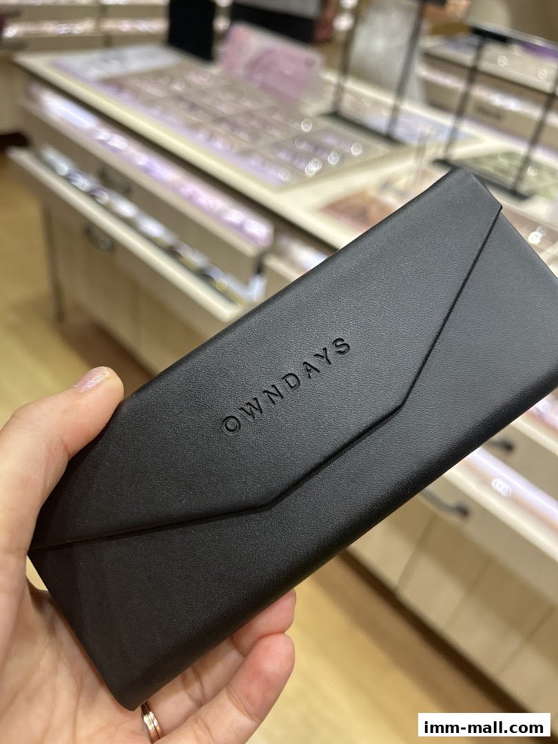 A hand holds a black OWNDAYS glasses case in front of a display of eyeglasses.