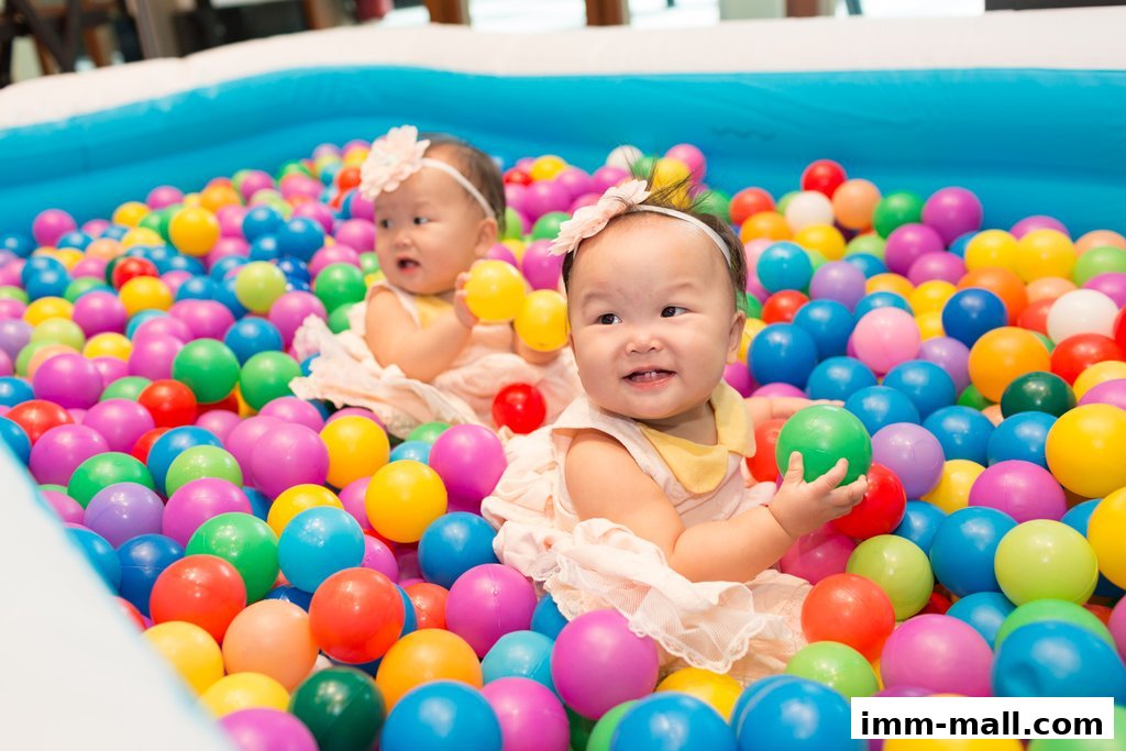 Two babies smiling and playing in a ball pit filled with colorful balls.
