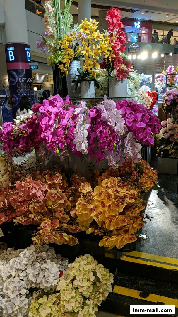 A vibrant display of artificial orchids and hydrangeas in various colors, arranged in pots.