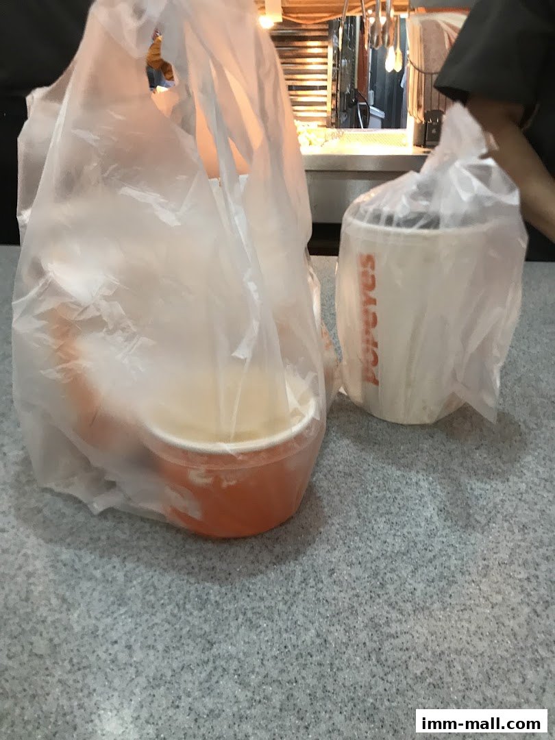 Two Popeyes takeout bags containing food items on a speckled table.