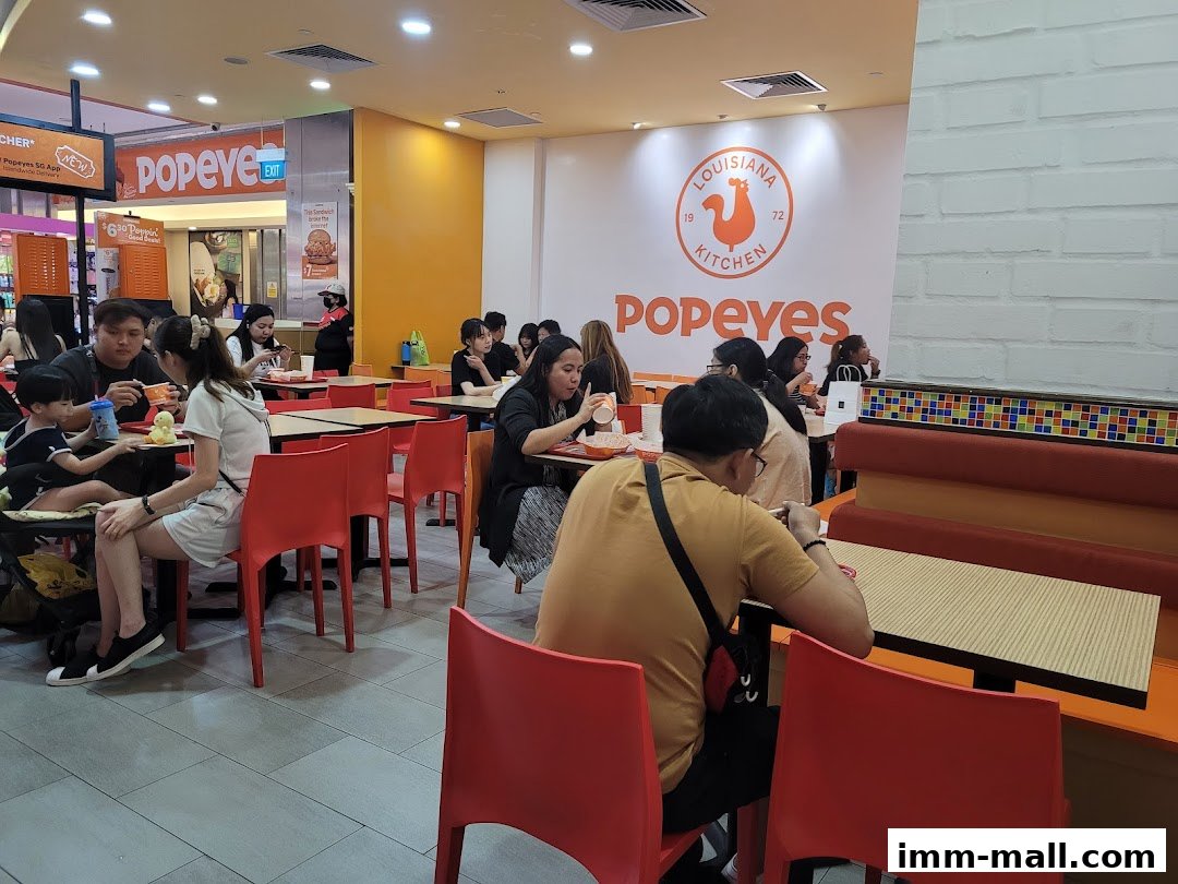 People dining at Popeyes restaurant with bright orange seating and the Popeyes logo on the wall.