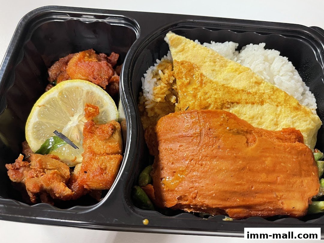 A close-up of a takeaway meal with rice, omelet, fried chicken, and vegetables.