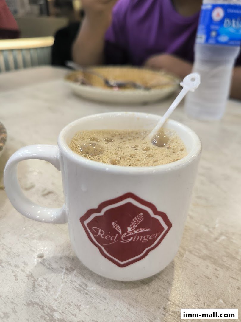 A close-up of a white mug with the Red Ginger logo, filled with a frothy beverage.