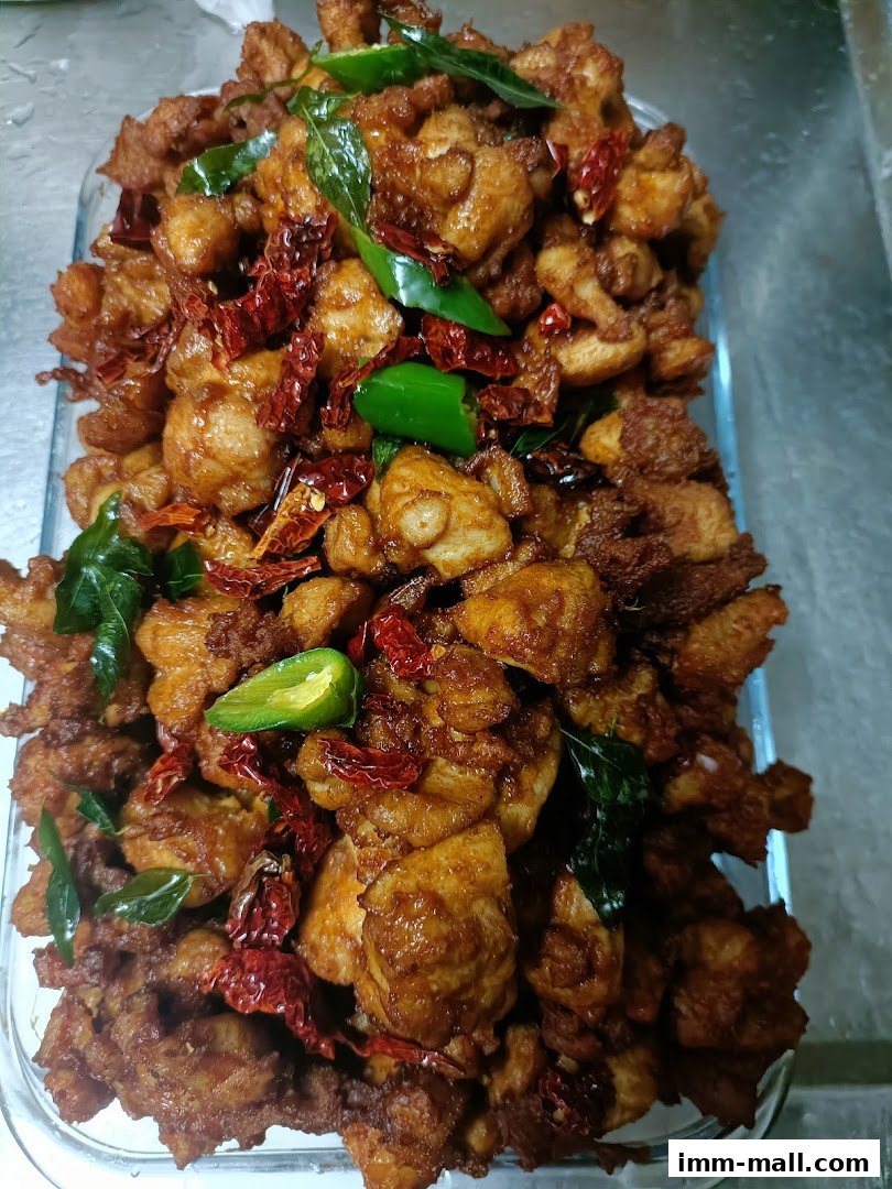 A close-up of a dish of crispy fried chicken pieces with chili peppers and curry leaves.
