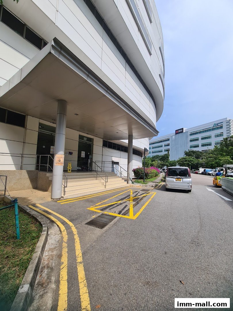 Exterior view of a modern building entrance with a silver van parked nearby.