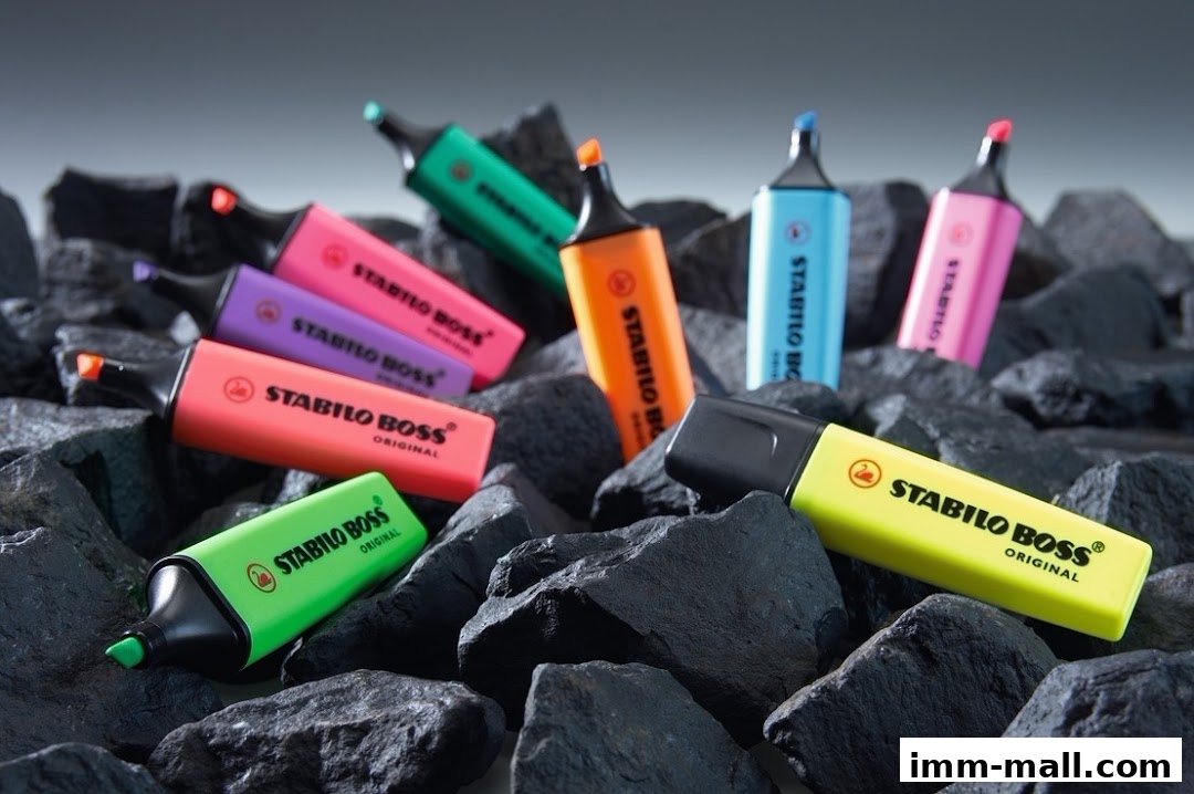 A collection of colorful STABILO BOSS highlighters scattered among dark rocks.