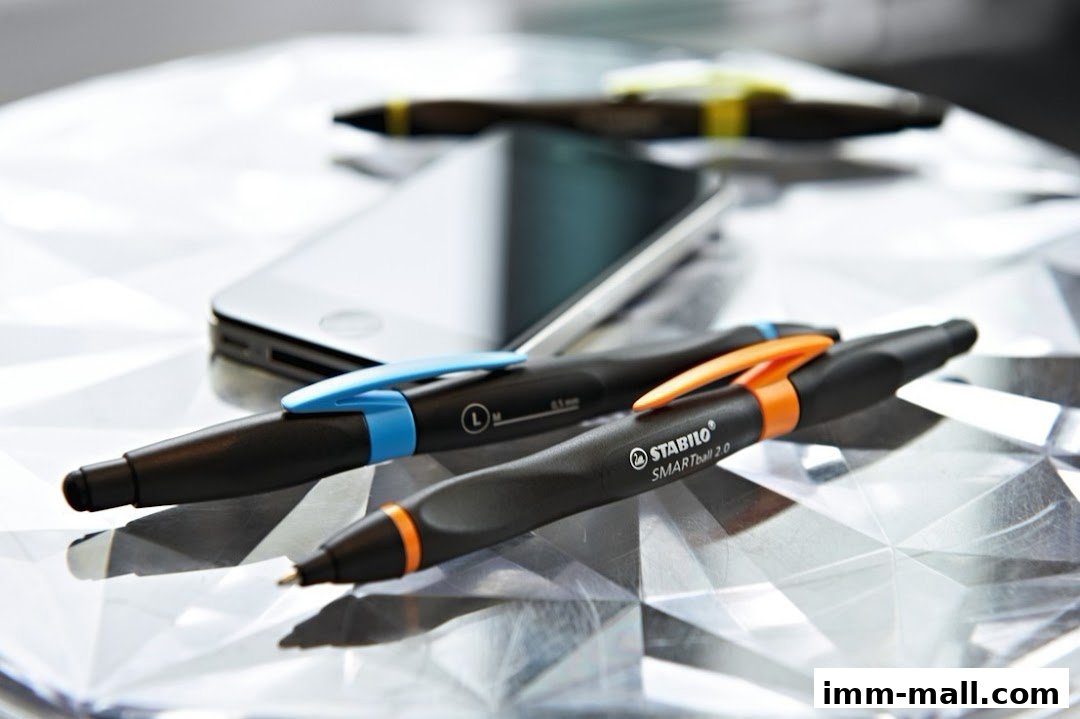 Close-up of two STABILO SMARTball 2.0 pens with a smartphone and other pens in the background.