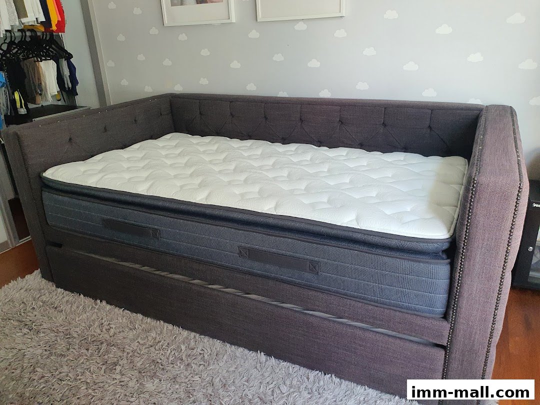 A tufted grey sofa bed with a white mattress on top, placed on a grey rug.