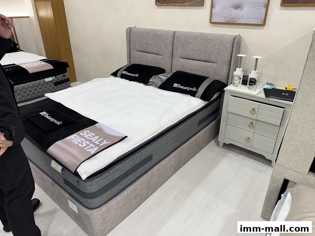 A Sealy Posturepedic mattress display with a bedside table and decorative items.