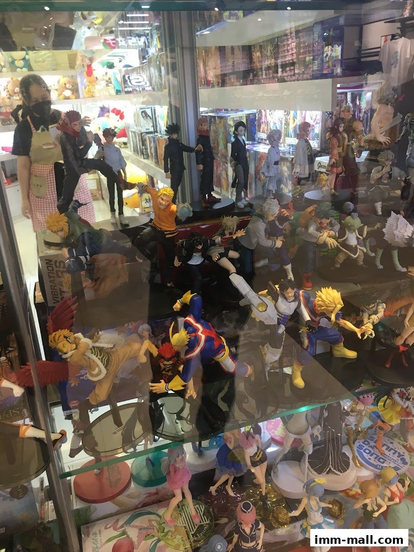 A display case filled with anime figurines and merchandise, with a staff member in the background.