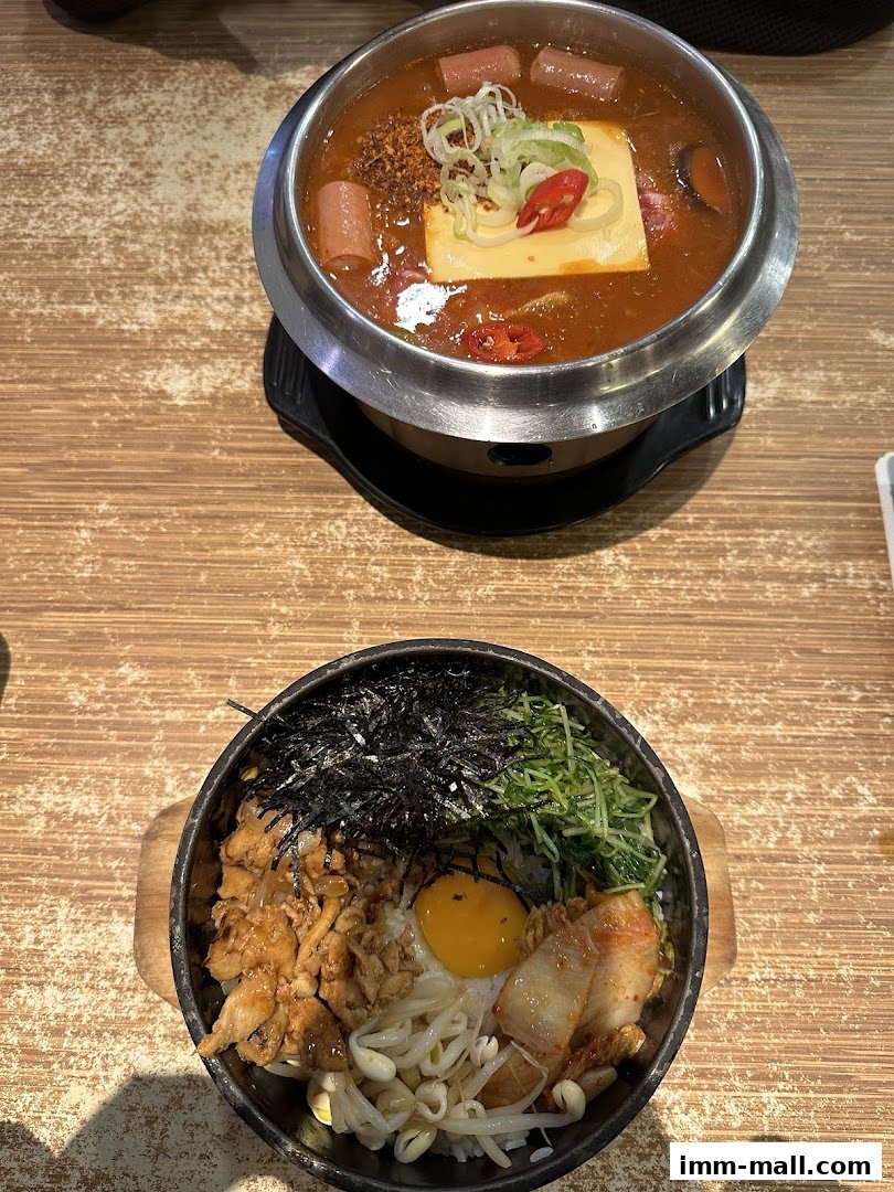 Two delicious Korean dishes, a hot pot and a bibimbap, are presented on a wooden table.