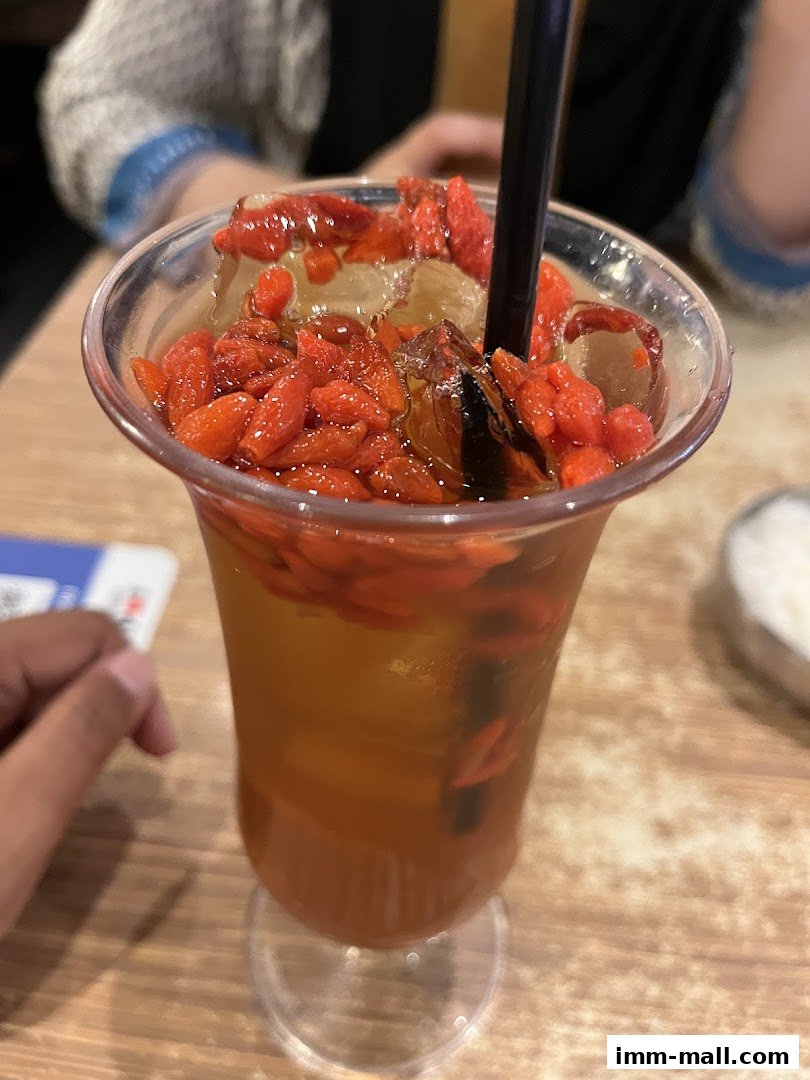 A refreshing drink with goji berries and ice in a clear cup with a straw.