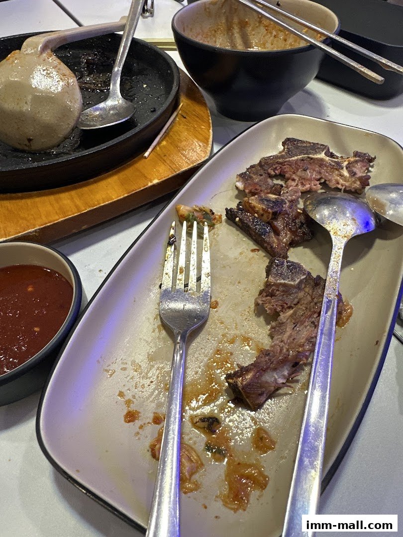 A table with leftover food, including ribs, a dipping sauce, and cutlery.