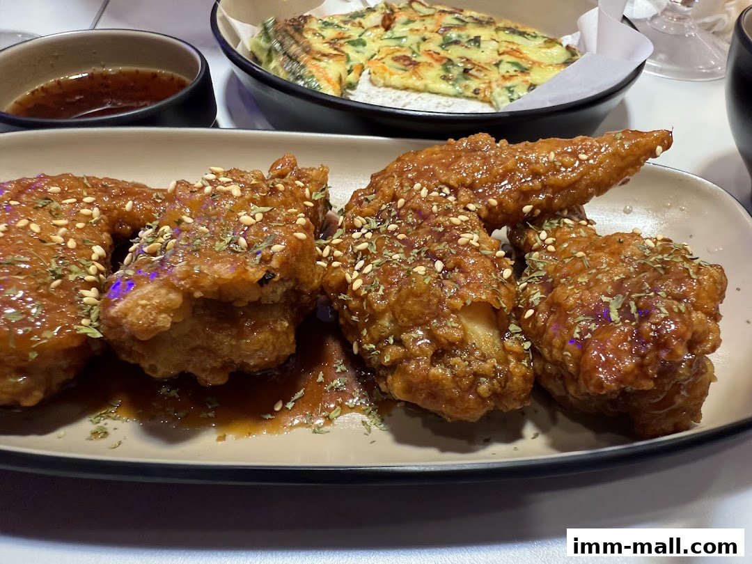 A plate of crispy, glazed chicken wings with sesame seeds and herbs, served with dipping sauce.