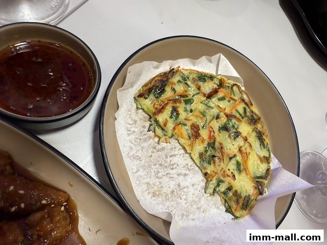 A close-up of a Korean pancake with dipping sauce and another dish.