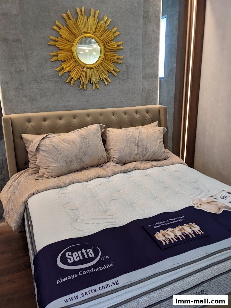 A Serta mattress display featuring a tufted headboard, pillows, and a decorative sunburst mirror.