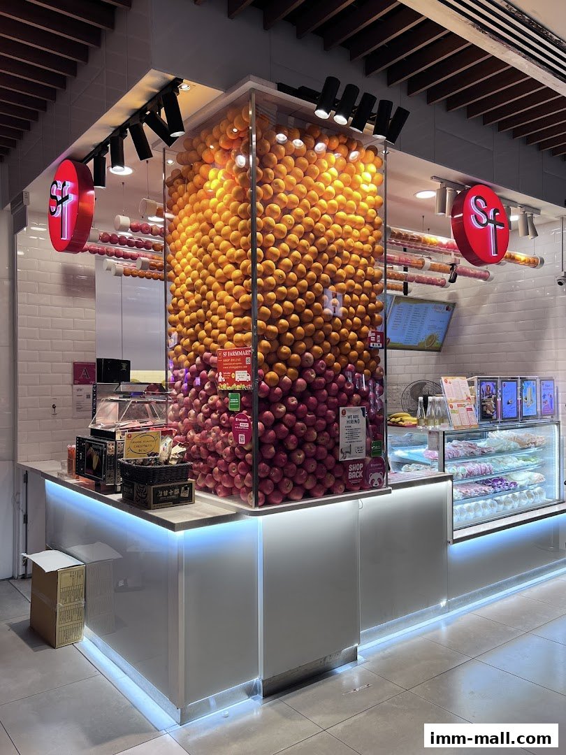 A brightly lit juice shop with a large display of oranges and apples, and a refrigerated case with desserts.