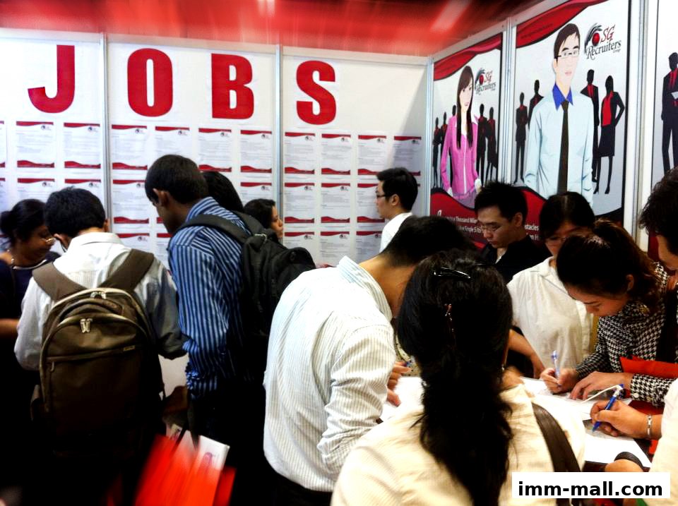 People gathered at a job fair, looking at job listings and filling out forms.