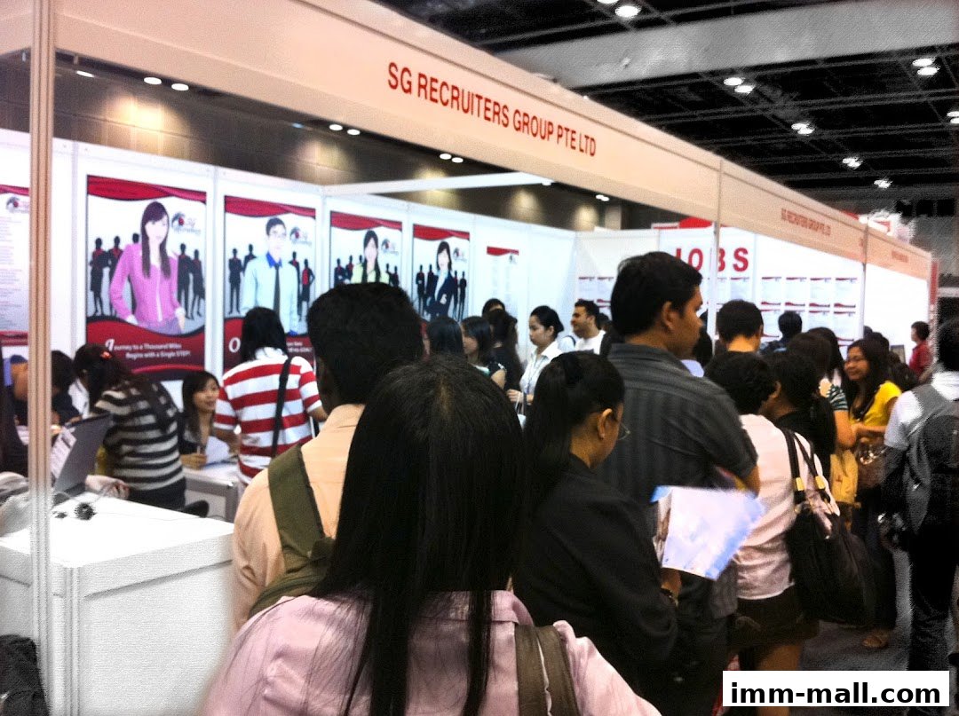 People queuing at a recruitment agency booth with company branding and job advertisements.
