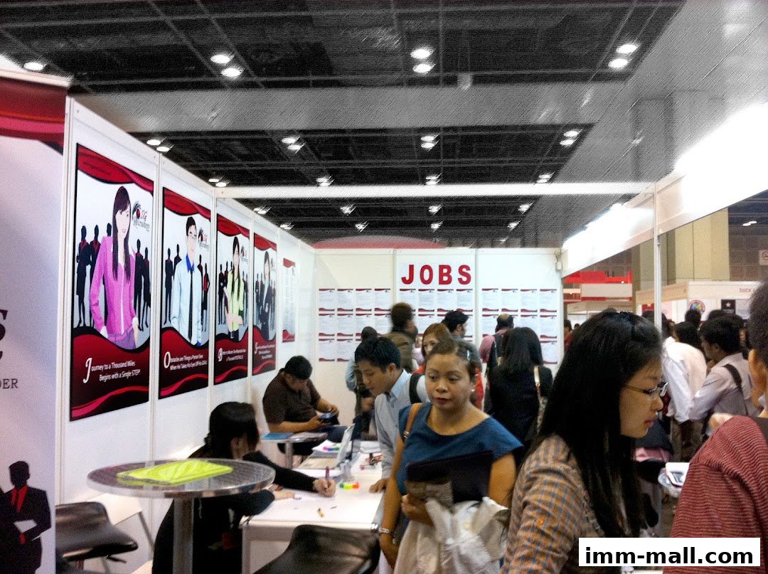 People at a job fair booth with 'JOBS' signage and recruitment posters.