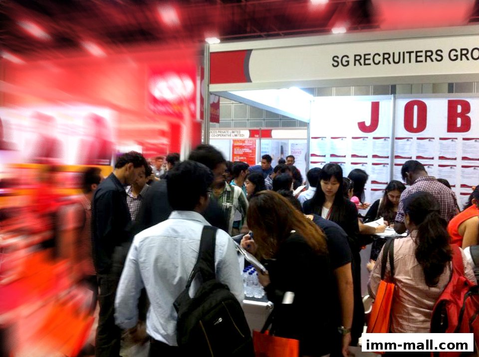 A busy recruitment event with people gathered around booths and job listings.