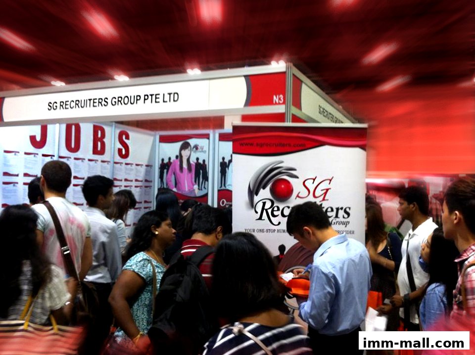 A busy recruitment fair booth with people looking at job listings and interacting with staff.