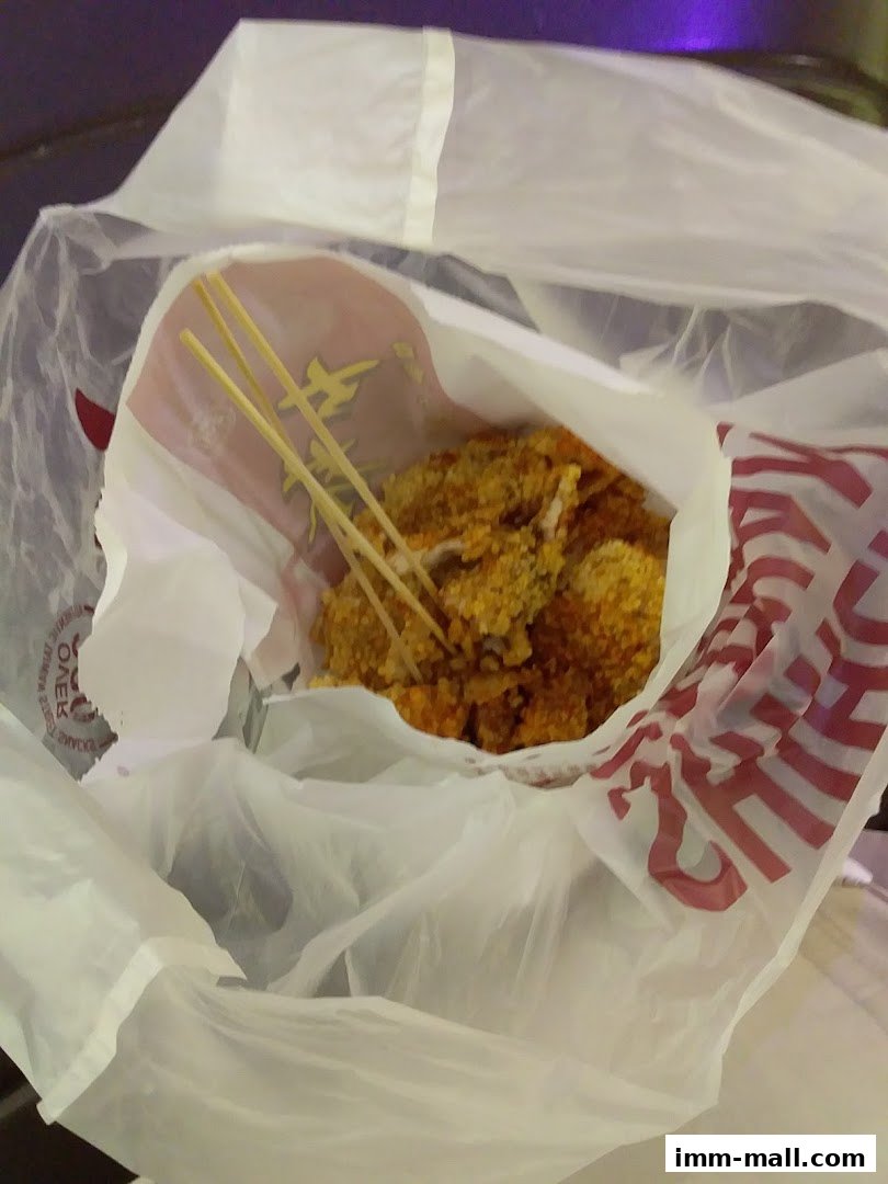 A white plastic bag filled with fried chicken pieces on skewers from Shihlin Taiwan Street Snacks.
