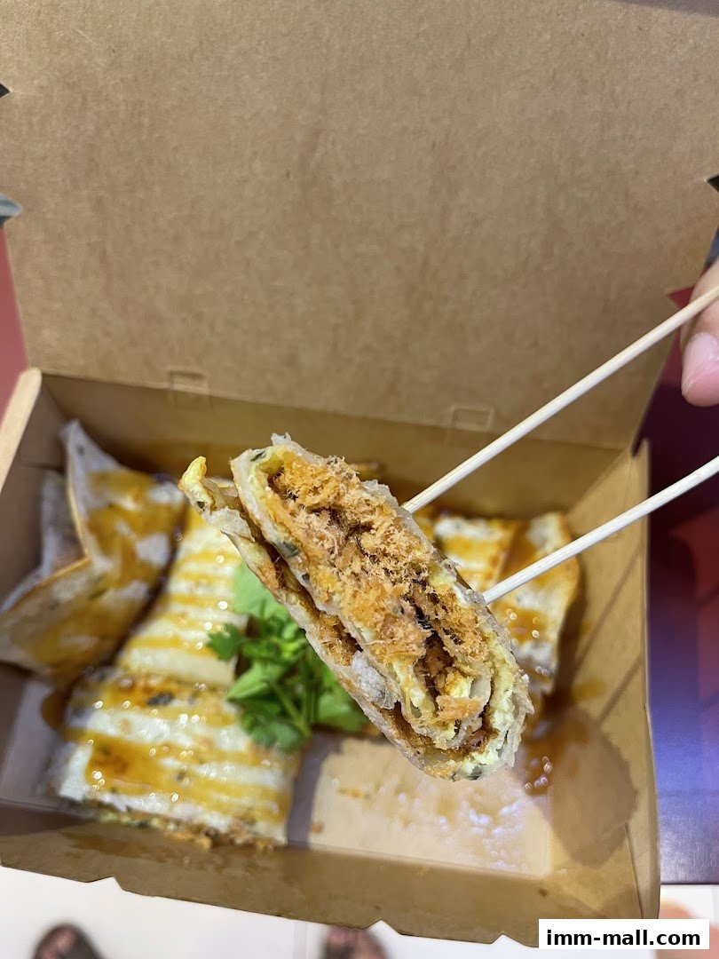 A close-up shot of a Taiwanese snack, likely a savory crepe, being held by chopsticks.