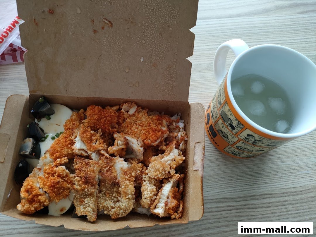 A takeout box filled with crispy fried chicken and rice, next to a mug of iced beverage.