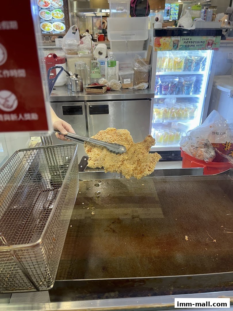A person is holding a large piece of fried chicken with tongs over a frying station.