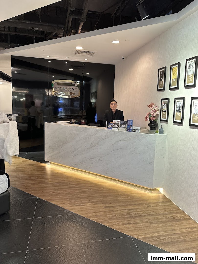 A man stands behind a marble reception desk in a modern shop with the Simmons logo.