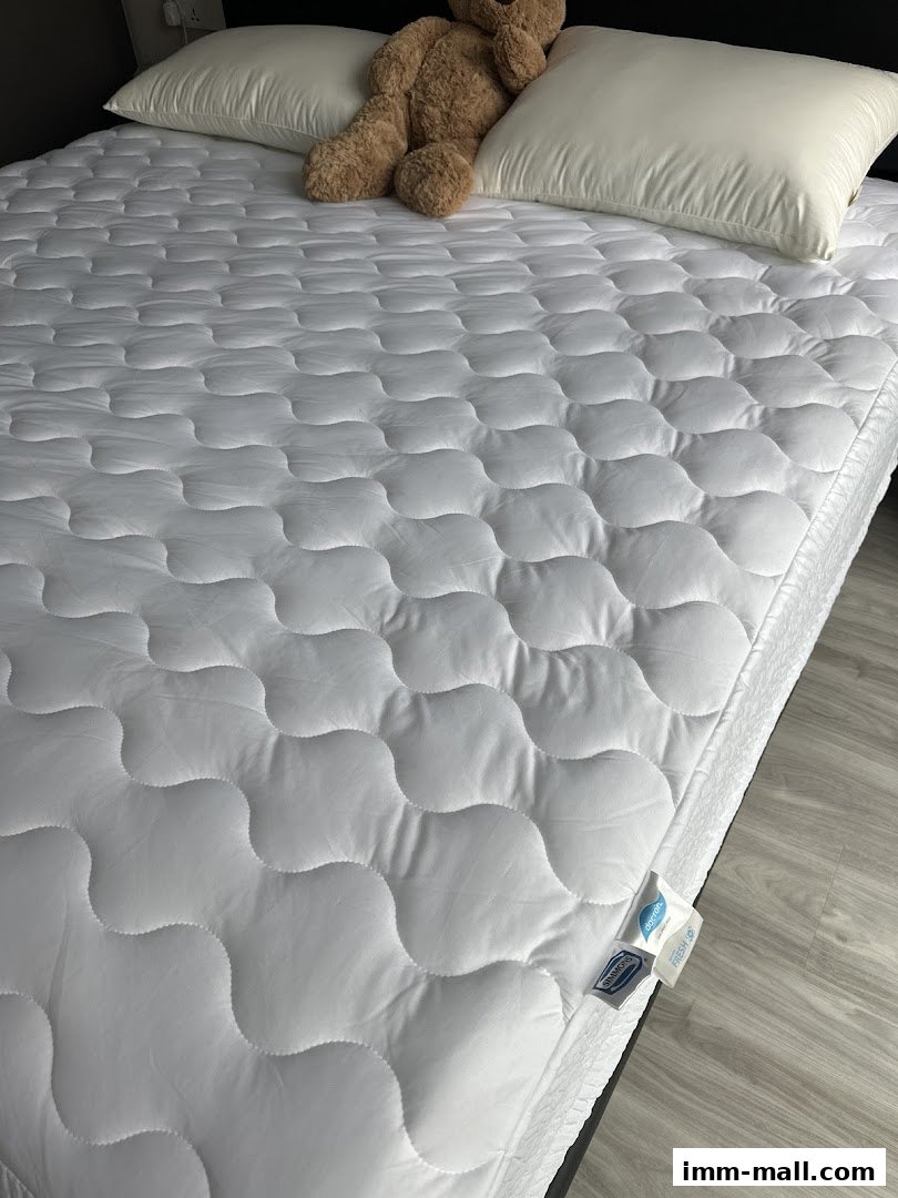 A white quilted mattress topper with a teddy bear and pillows on a bed.