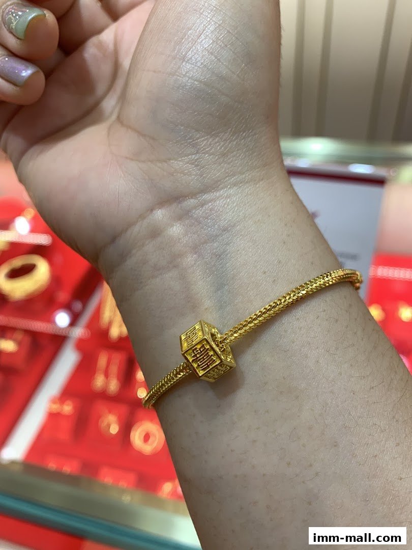 A close-up of a gold bracelet with a cubic charm featuring Chinese characters.