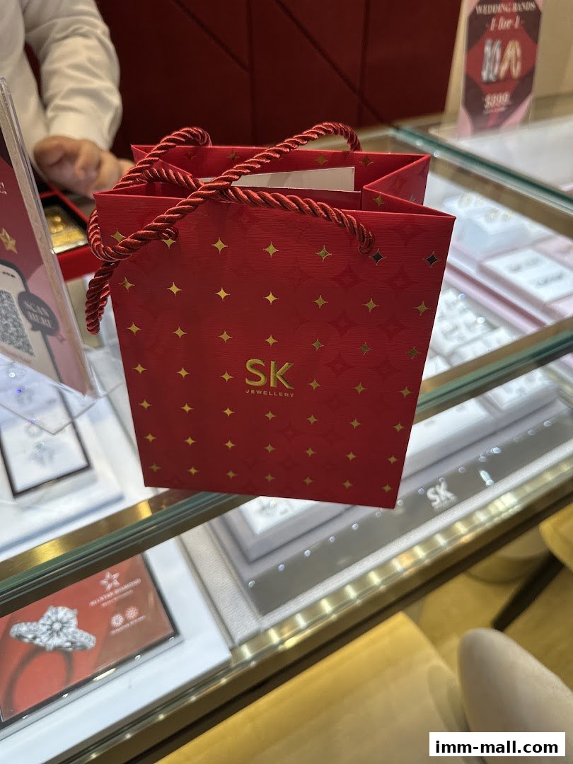 A red SK Jewellery shopping bag sits on a display case with jewelry inside.