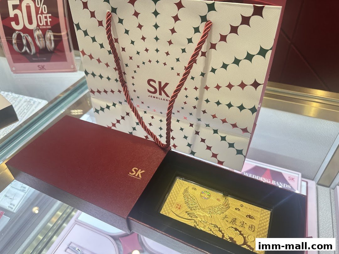 SK Jewellery display featuring a gold bar in a gift box and branded shopping bag.