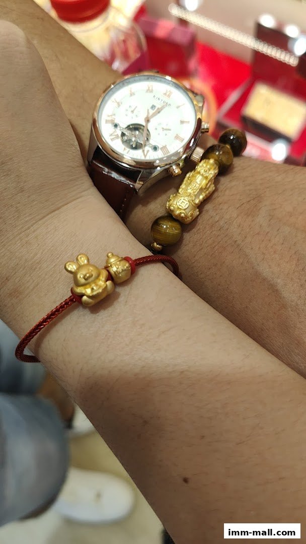 Close-up of two wrists wearing bracelets and a watch, with a blurred background of a jewelry store.