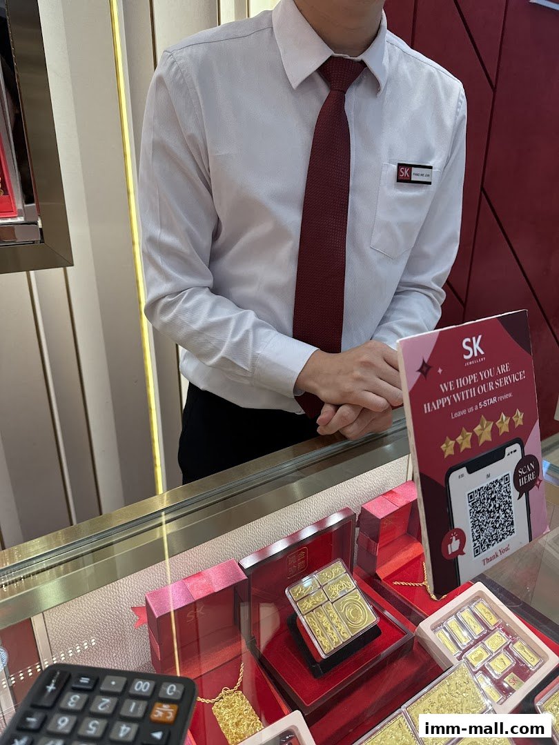 A store employee stands behind a display case filled with gold jewelry and bars.