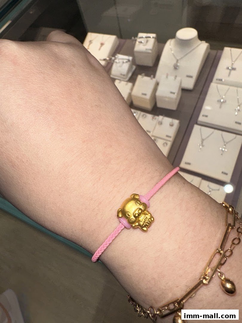 A hand wearing a gold pig charm bracelet with other jewelry displayed in the background.