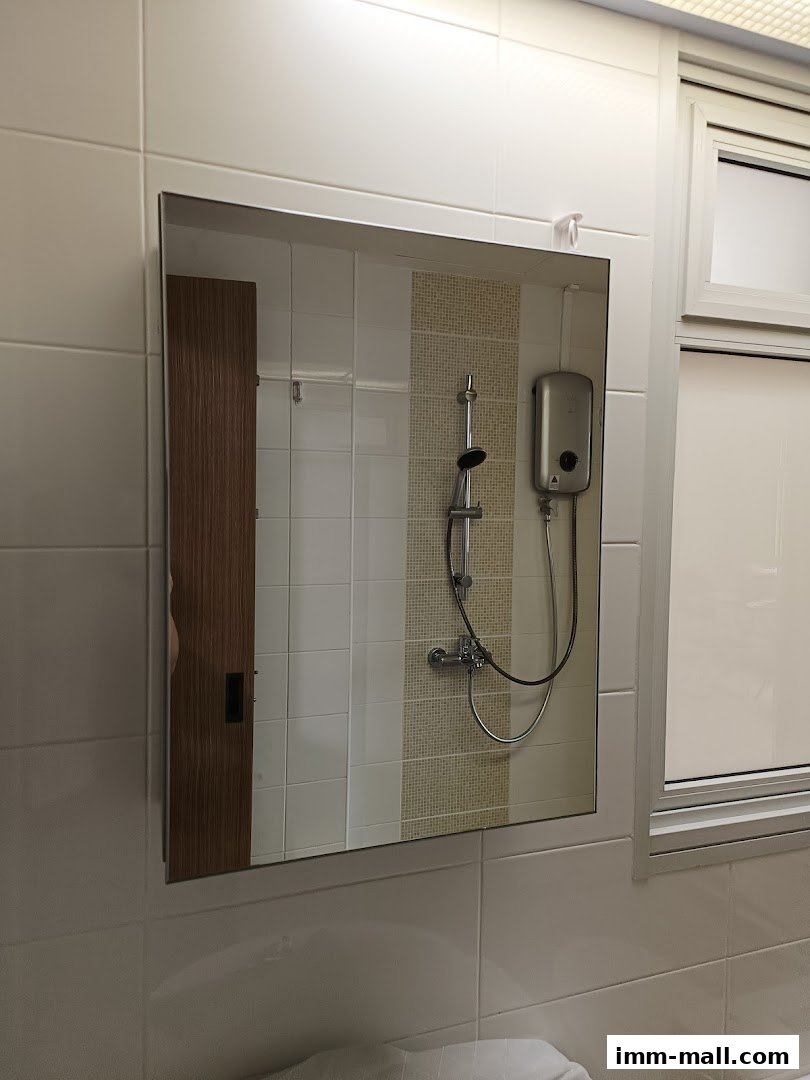 A bathroom mirror reflects a shower head, water heater, and tiled walls.