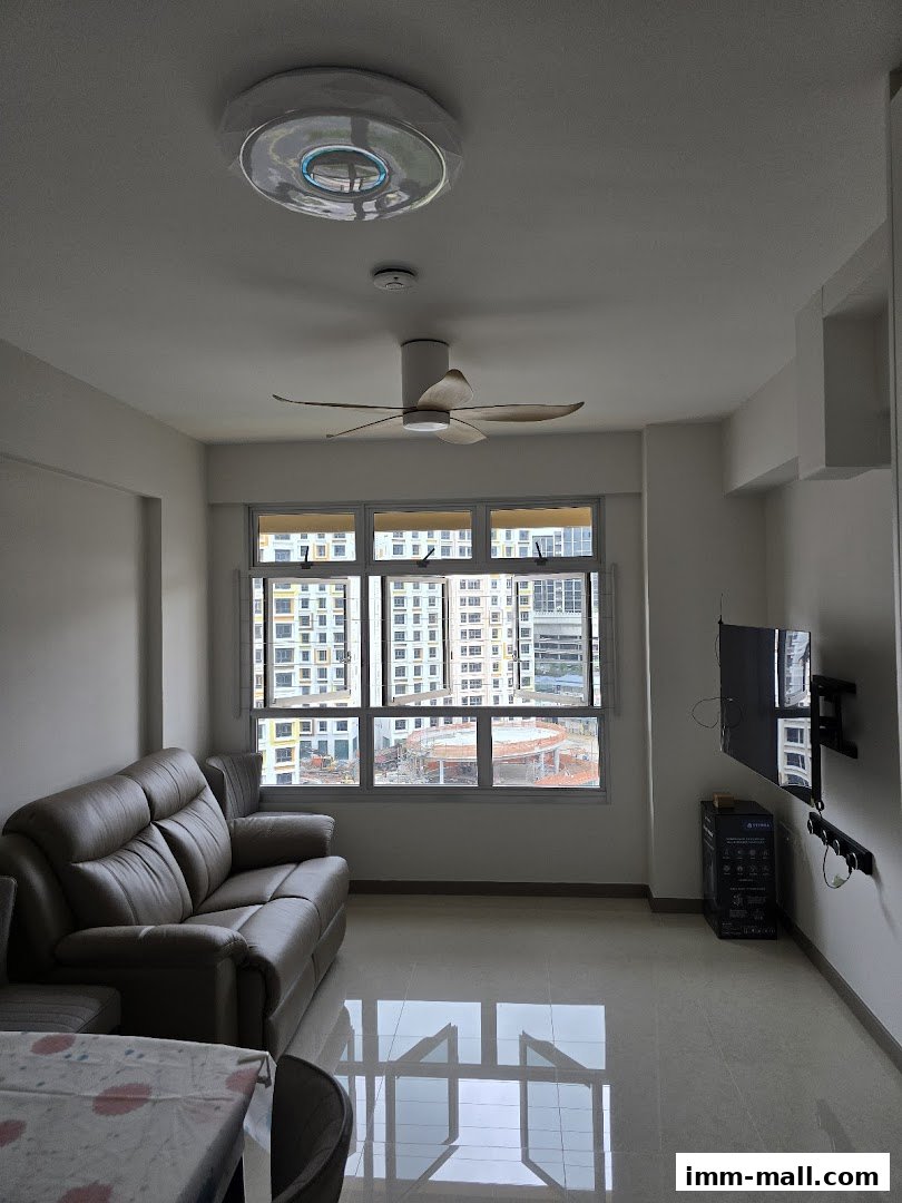 A living room with a sofa, TV, ceiling fan, and a large window overlooking a city view.
