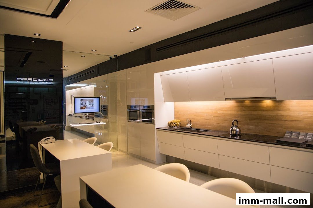 A modern, spacious kitchen showroom with sleek white cabinetry and integrated appliances.